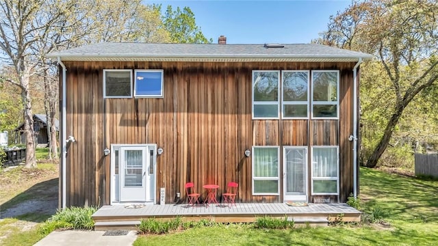 back of property with a wooden deck, a chimney, a lawn, and a shingled roof