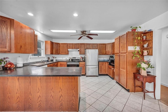 kitchen featuring stainless steel appliances, a peninsula, dark countertops, brown cabinetry, and recessed lighting