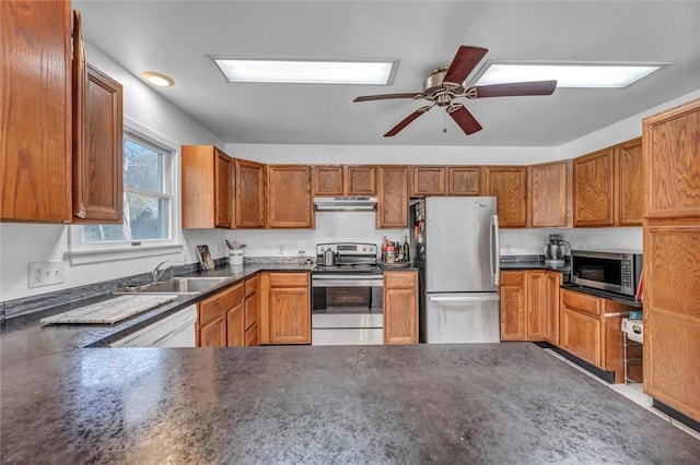 kitchen with appliances with stainless steel finishes, a sink, under cabinet range hood, dark countertops, and a ceiling fan