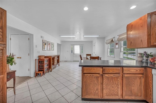 kitchen with a peninsula, dark countertops, light tile patterned floors, brown cabinetry, and dishwasher