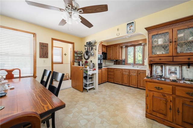 kitchen with brown cabinetry, ceiling fan, arched walkways, a sink, and black oven