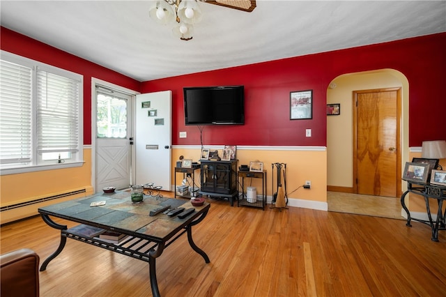 living area featuring arched walkways, wood finished floors, a baseboard heating unit, a ceiling fan, and baseboards