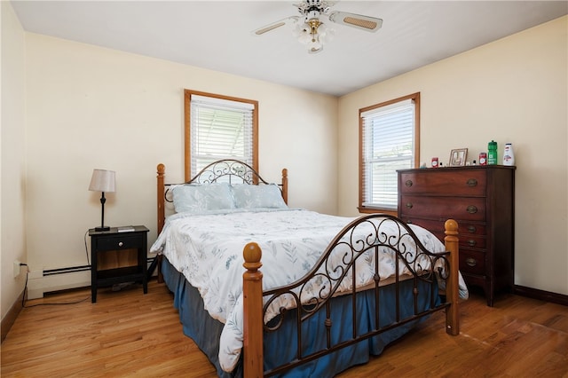bedroom featuring wood finished floors, a baseboard radiator, baseboards, and a ceiling fan