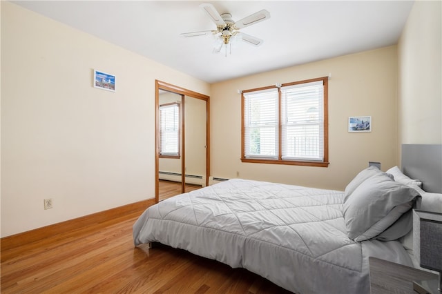bedroom with a closet, wood finished floors, baseboard heating, and a ceiling fan