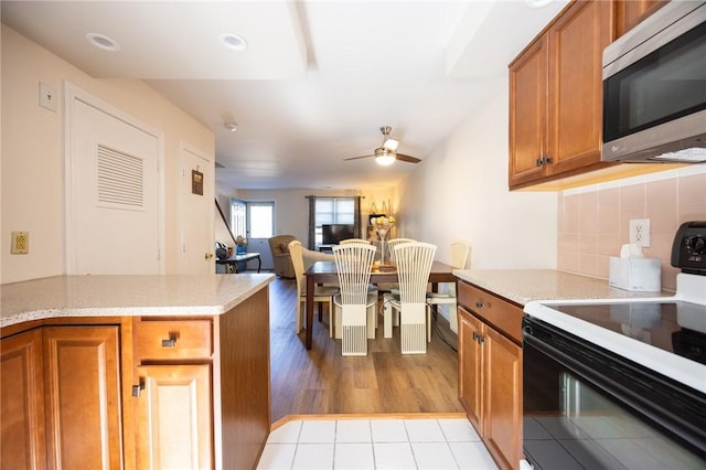 3399 Post Rd Unit 7, Warwick, RI 02886 - kitchen with stainless steel microwave, black electric range oven, brown cabinetry, ceiling fan, and tasteful backsplash