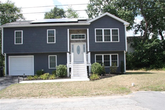 raised ranch featuring a garage, solar panels, asphalt driveway, and a front yard