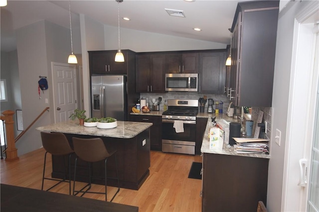 kitchen with appliances with stainless steel finishes, backsplash, lofted ceiling, dark brown cabinetry, and a kitchen island