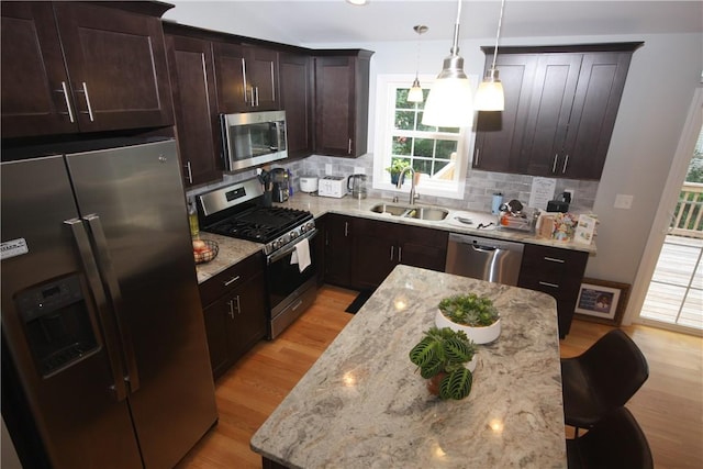 kitchen with appliances with stainless steel finishes, a sink, light wood-style flooring, backsplash, and light stone counters