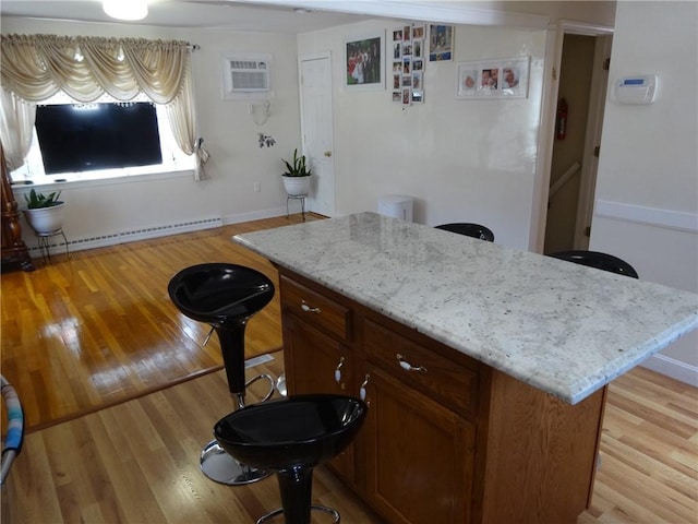 kitchen featuring a baseboard radiator, a wall mounted AC, light wood finished floors, a center island, and light stone counters