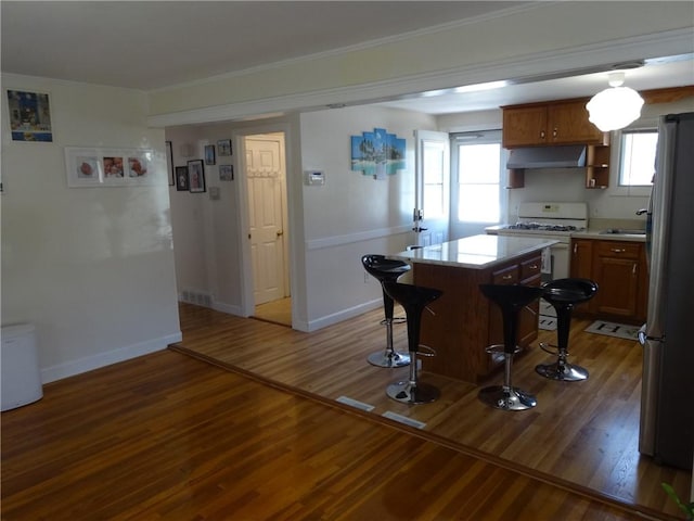 kitchen featuring white range with gas cooktop, under cabinet range hood, a breakfast bar, freestanding refrigerator, and crown molding