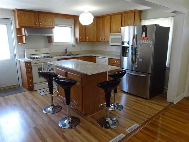 kitchen with white appliances, under cabinet range hood, a kitchen bar, brown cabinets, and a kitchen island