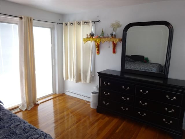bedroom featuring multiple windows, wood finished floors, and a baseboard heating unit