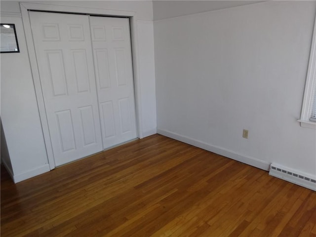 unfurnished bedroom featuring wood finished floors, a closet, baseboards, and a baseboard radiator