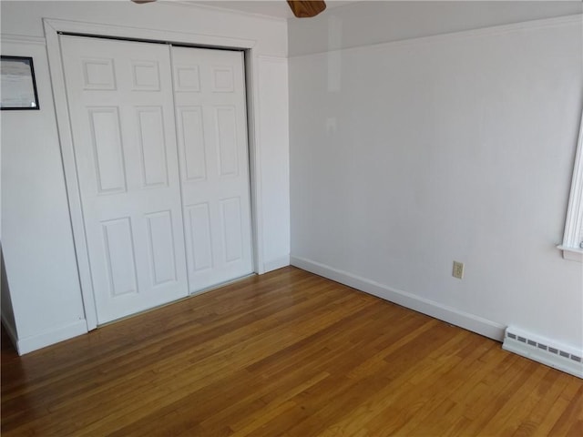 unfurnished bedroom featuring wood finished floors, baseboards, a closet, and a ceiling fan