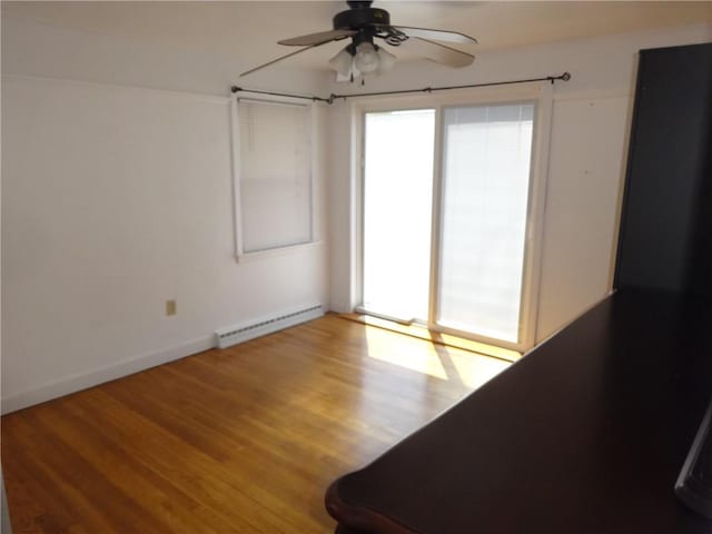 spare room featuring baseboard heating, healthy amount of natural light, ceiling fan, and wood finished floors