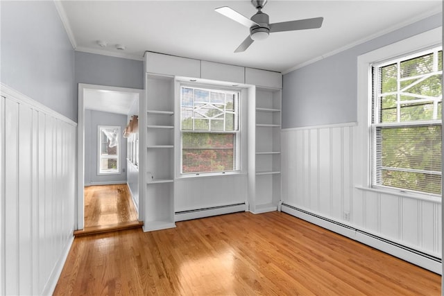 unfurnished room with a baseboard radiator, light wood-style floors, crown molding, a wainscoted wall, and a ceiling fan