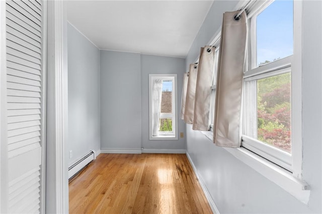empty room with a baseboard radiator, light wood finished floors, and baseboards