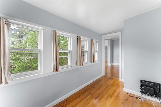 corridor with baseboards, light wood finished floors, and vaulted ceiling