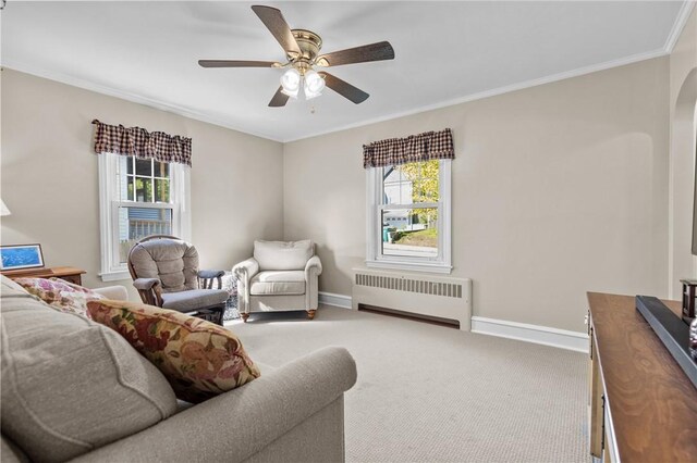 carpeted living room featuring radiator, baseboards, ornamental molding, ceiling fan, and arched walkways