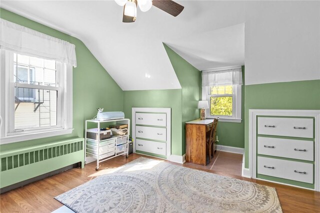 bedroom with radiator, lofted ceiling, baseboards, wood finished floors, and ceiling fan
