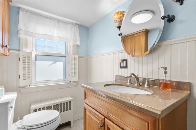 half bathroom featuring radiator heating unit, toilet, a wainscoted wall, vanity, and a decorative wall
