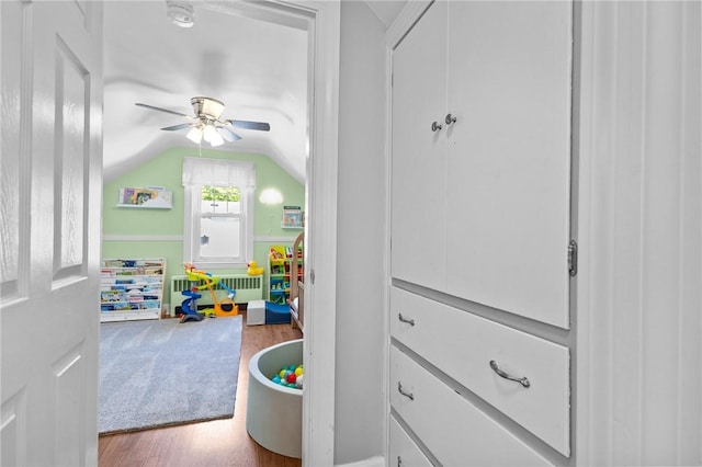 rec room with radiator, wood finished floors, a ceiling fan, and vaulted ceiling