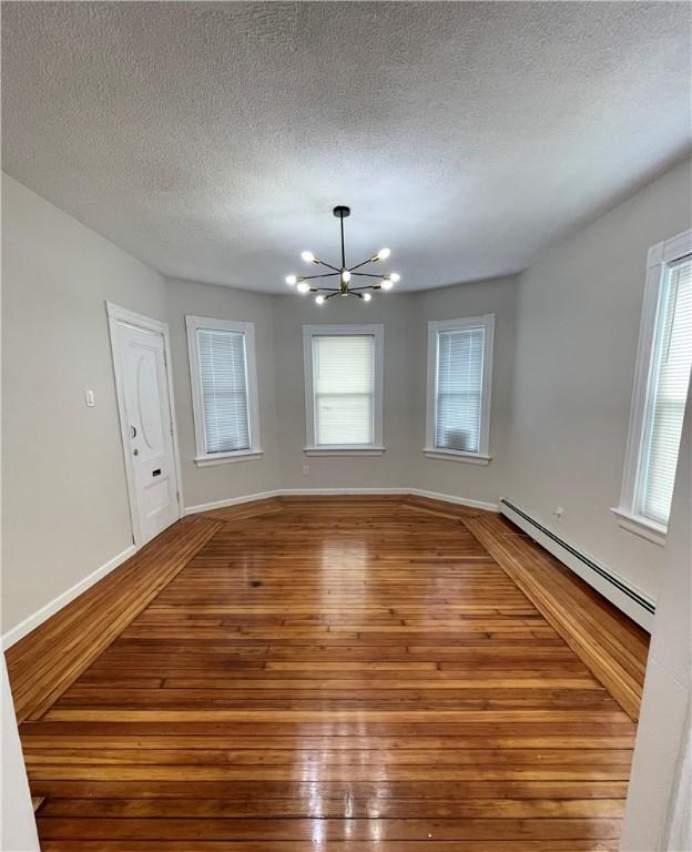 unfurnished dining area with a baseboard radiator, wood-type flooring, a chandelier, a textured ceiling, and baseboards