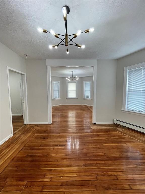 spare room featuring a chandelier, hardwood / wood-style flooring, a textured ceiling, baseboards, and a baseboard radiator