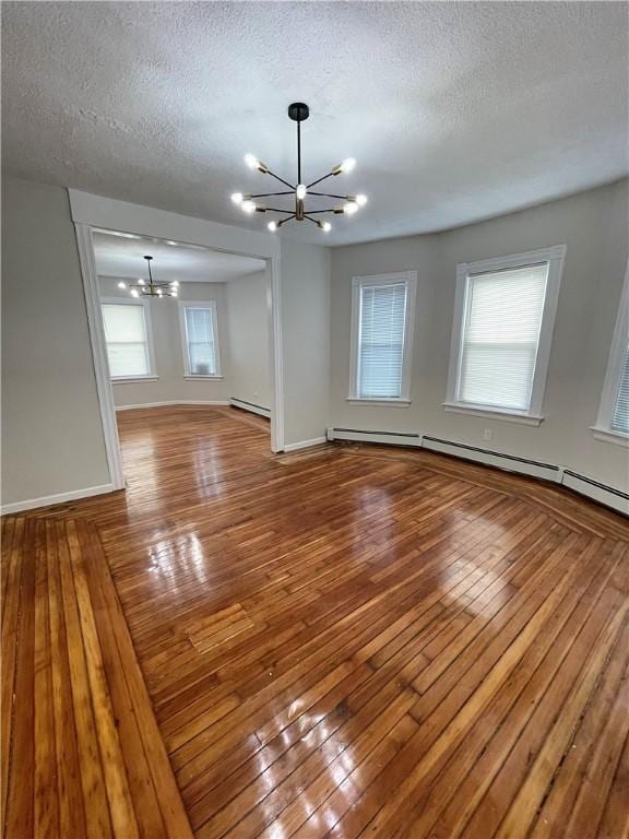 empty room featuring a chandelier, a textured ceiling, hardwood / wood-style flooring, a baseboard heating unit, and baseboards