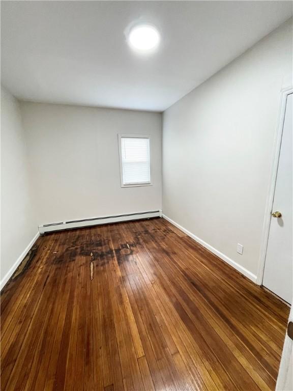 spare room featuring a baseboard radiator, baseboards, and wood-type flooring