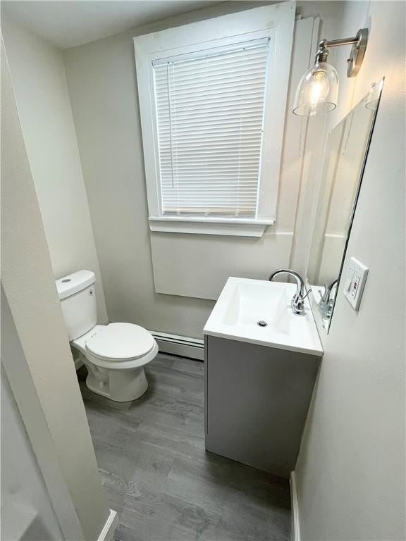 half bath featuring a baseboard radiator, vanity, toilet, wood finished floors, and baseboards