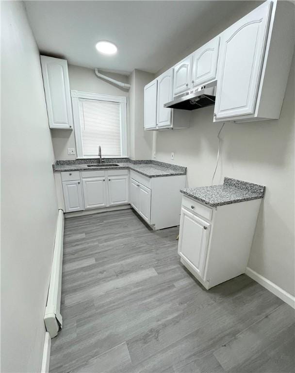 kitchen with under cabinet range hood, white cabinetry, a sink, light wood-style floors, and light stone countertops