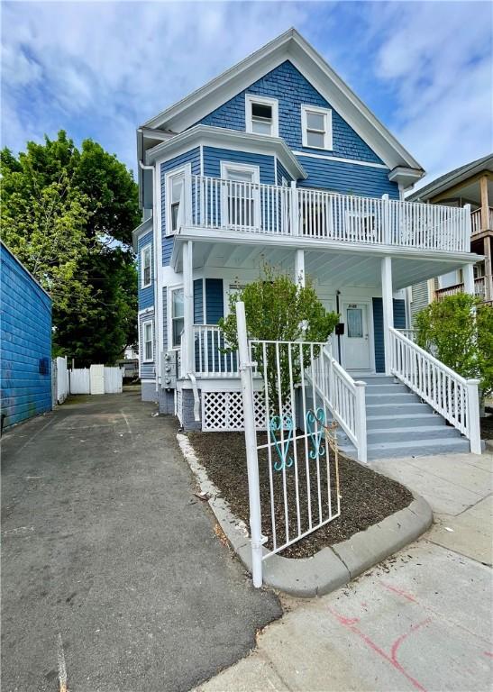 view of front of house featuring covered porch, a balcony, stairway, and asphalt driveway