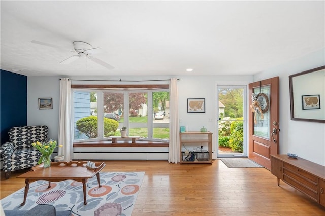 living room with light wood finished floors, a baseboard heating unit, and a ceiling fan