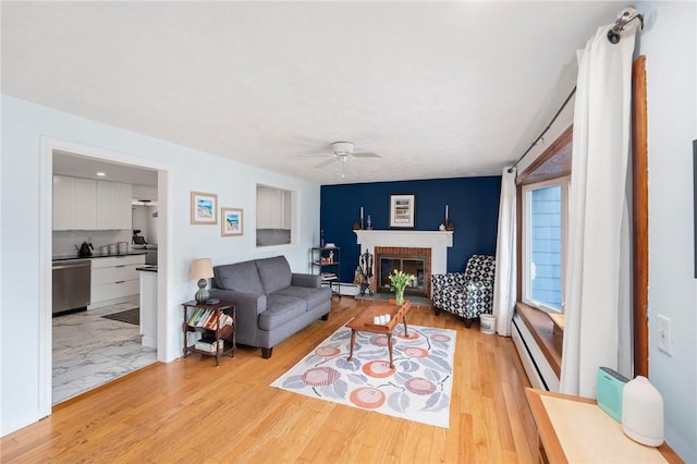 living area featuring a baseboard radiator, a ceiling fan, light wood-style floors, a brick fireplace, and a baseboard heating unit