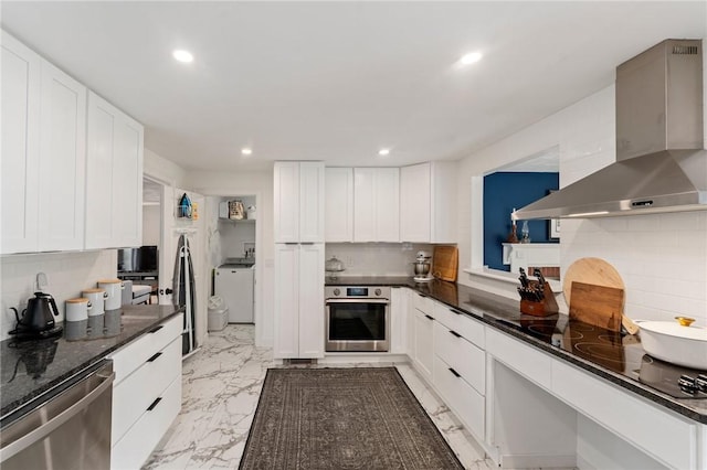 kitchen featuring stainless steel appliances, wall chimney range hood, washer / dryer, recessed lighting, and backsplash