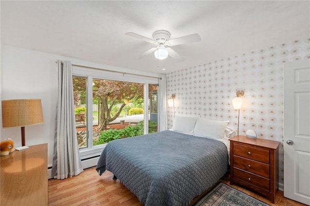 bedroom with wallpapered walls, light wood-style flooring, a baseboard heating unit, and ceiling fan