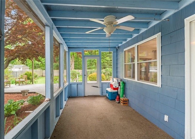 unfurnished sunroom featuring ceiling fan, plenty of natural light, and beamed ceiling