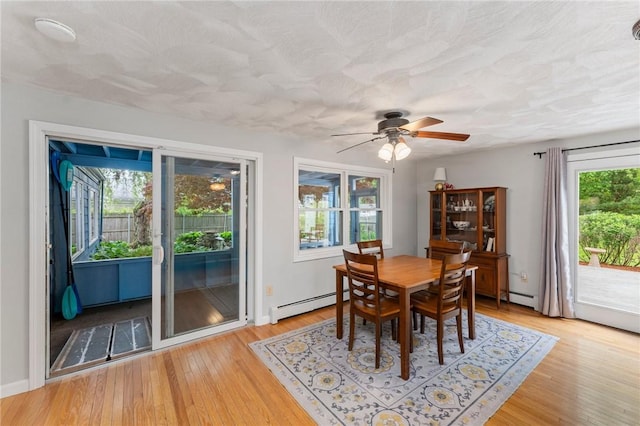 dining room featuring a baseboard heating unit, light wood-style floors, a ceiling fan, and baseboards