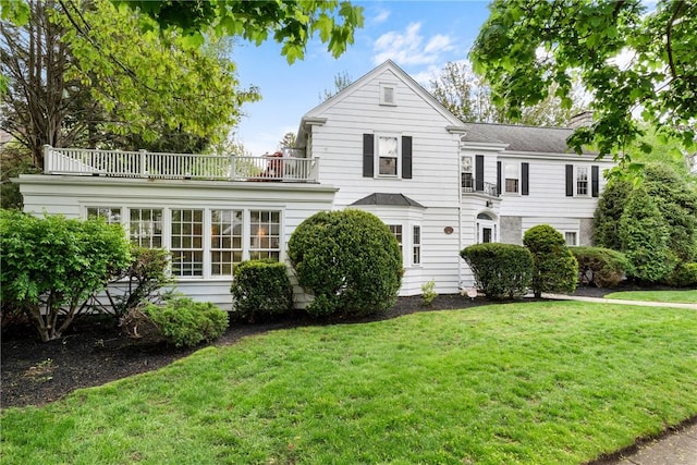 view of front of home with a balcony, a front lawn, and a chimney