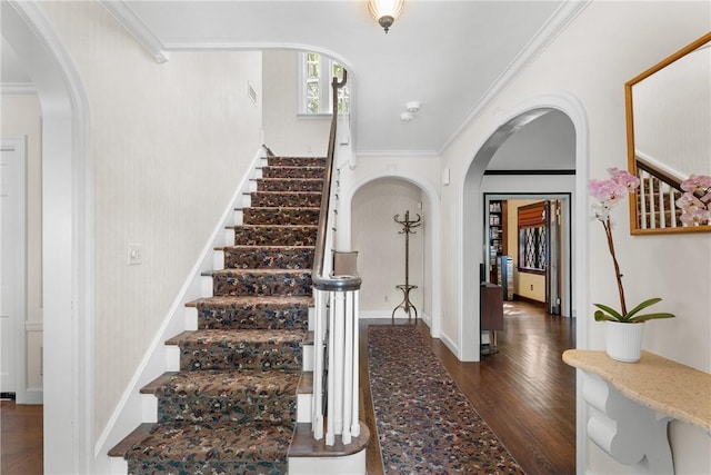 foyer entrance featuring dark wood-style floors, arched walkways, stairway, crown molding, and baseboards