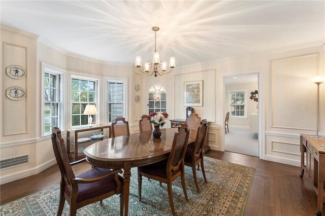 dining room with a chandelier, dark wood-type flooring, ornamental molding, baseboards, and a decorative wall