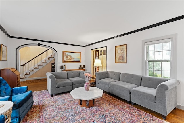 living room featuring crown molding, wood finished floors, stairs, baseboards, and arched walkways