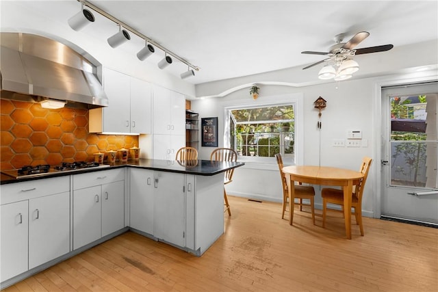 kitchen with stainless steel gas stovetop, dark countertops, a peninsula, ceiling fan, and light wood-style flooring