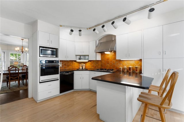kitchen featuring stainless steel appliances, wall chimney exhaust hood, a peninsula, dark countertops, and a chandelier