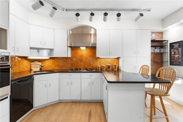 kitchen with a sink, wall chimney range hood, open shelves, a peninsula, and light wood-style floors