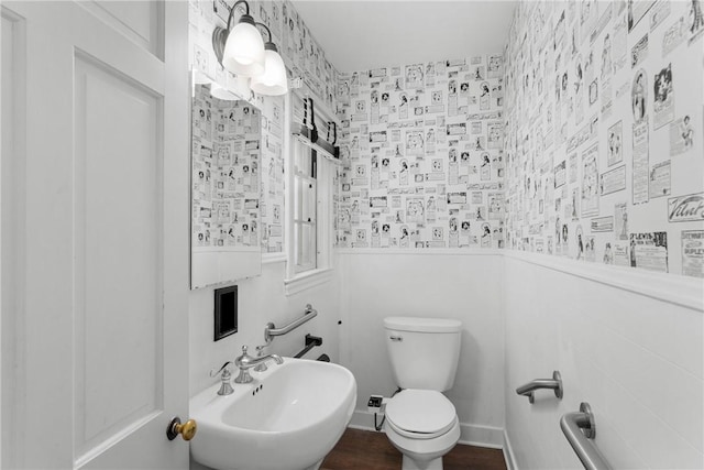 bathroom with a sink, toilet, wallpapered walls, and wood finished floors
