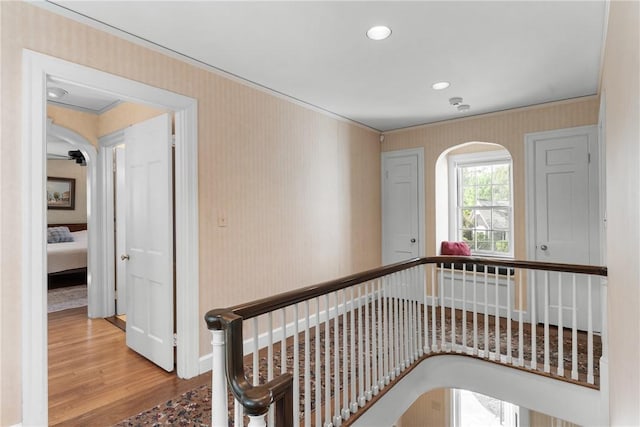 hall featuring arched walkways, wood finished floors, wallpapered walls, baseboards, and ornamental molding