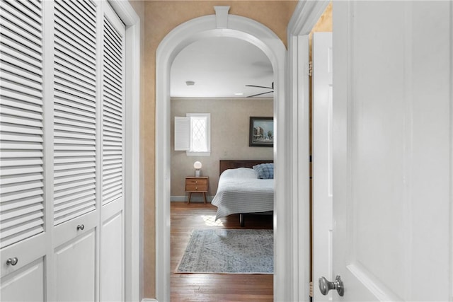 corridor with wood finished floors, arched walkways, and baseboards