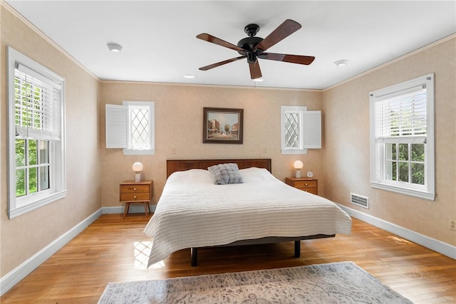 bedroom featuring ornamental molding, multiple windows, light wood-style floors, baseboards, and ceiling fan